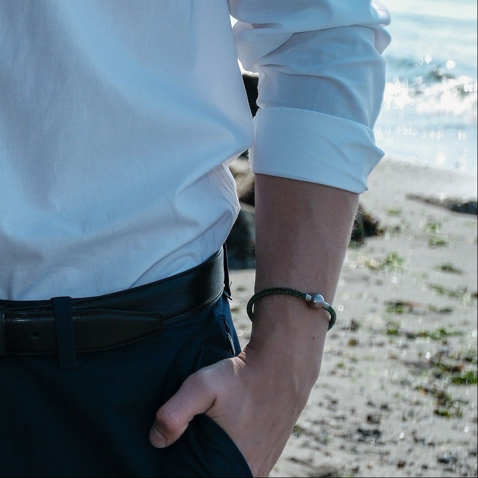 Man wearing a white shirt and black pants standing on a beach.