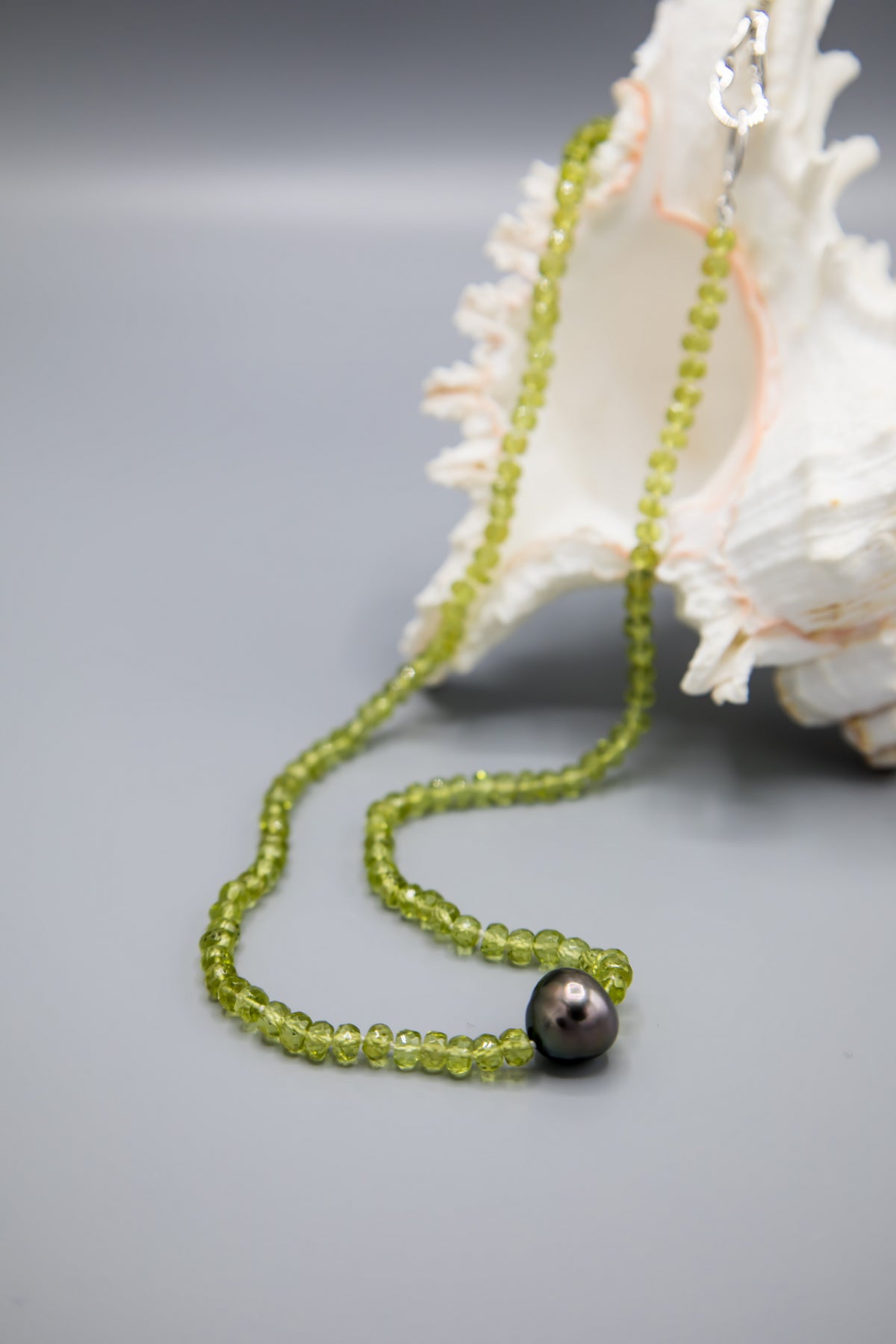 Peridot & Tahitian Pearl Necklace draped beside a seashell, with a close view of the pearl