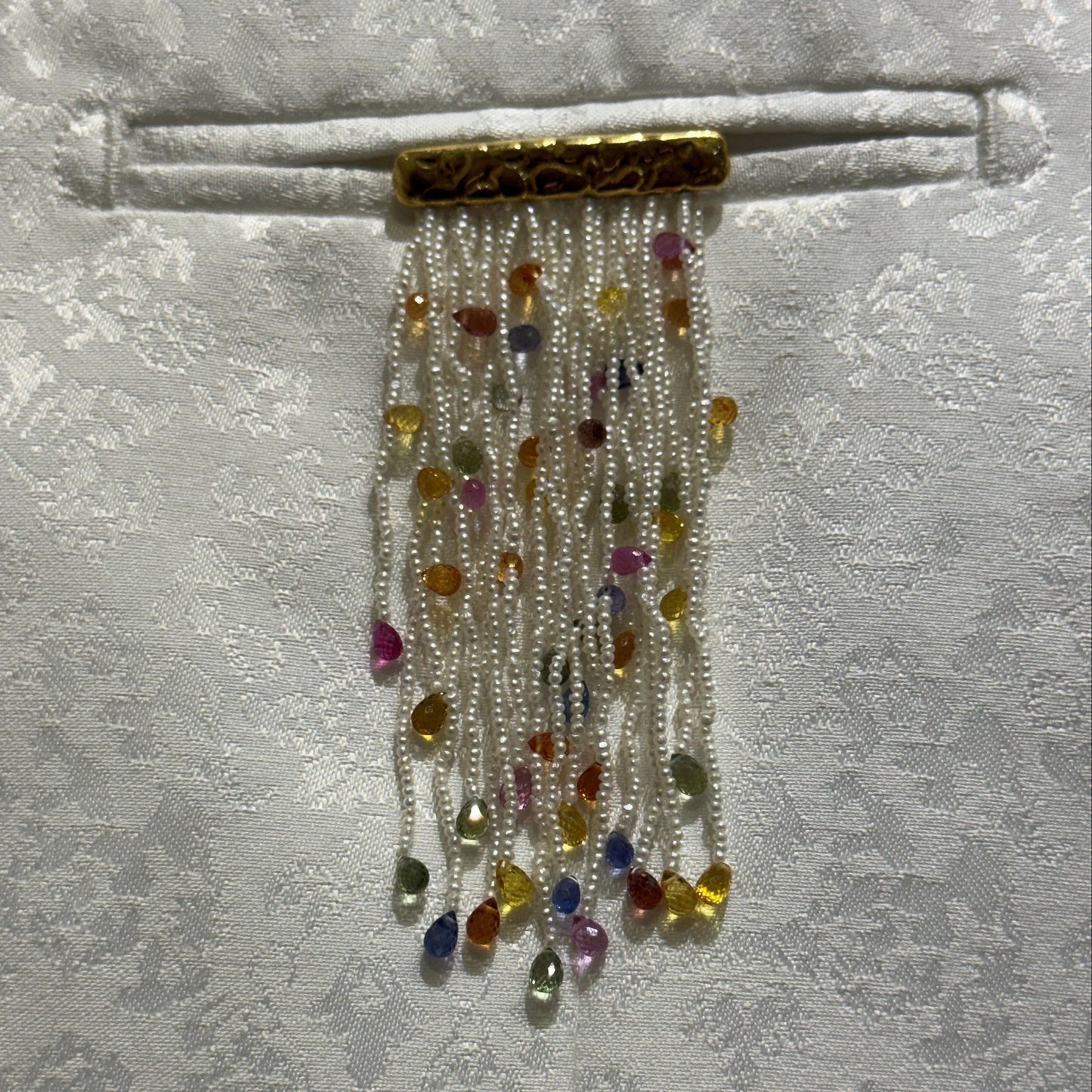 Akoya Keshi pearl fringe brooch with ruby and sapphire briolettes pinned to white silk fabric