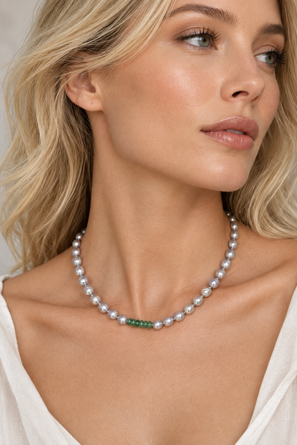 Model wearing a silver-grey baroque Akoya pearl necklace with faceted green emerald rondelle beads.