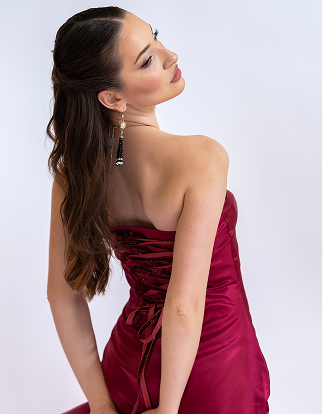 A woman wearing a strapless deep magenta satin dress, shown from a three-quarters back view against a light gray studio background.