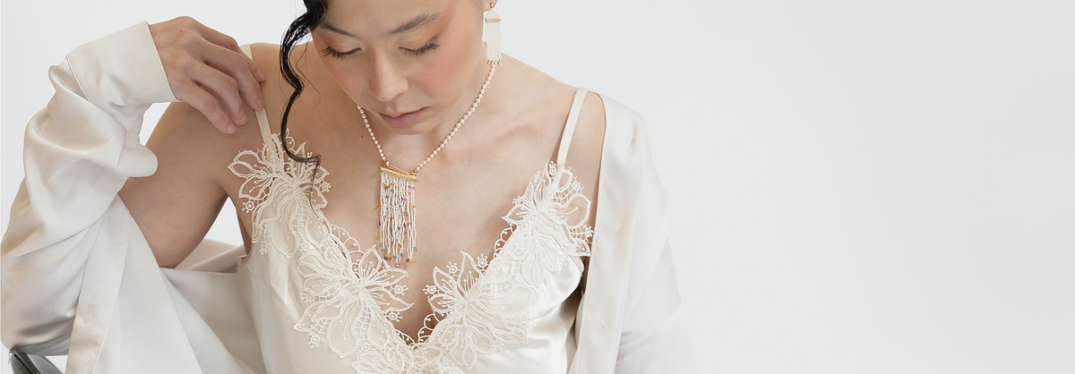 Woman wearing a pearl necklace with a multicolored beaded pendant over a white lace-trimmed dress.