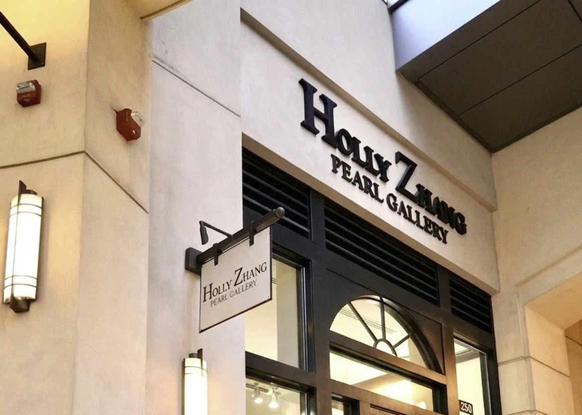 Storefront exterior of Holly Zhang Pearl Gallery featuring black dimensional wall signage and a matching hanging blade sign above the entrance.