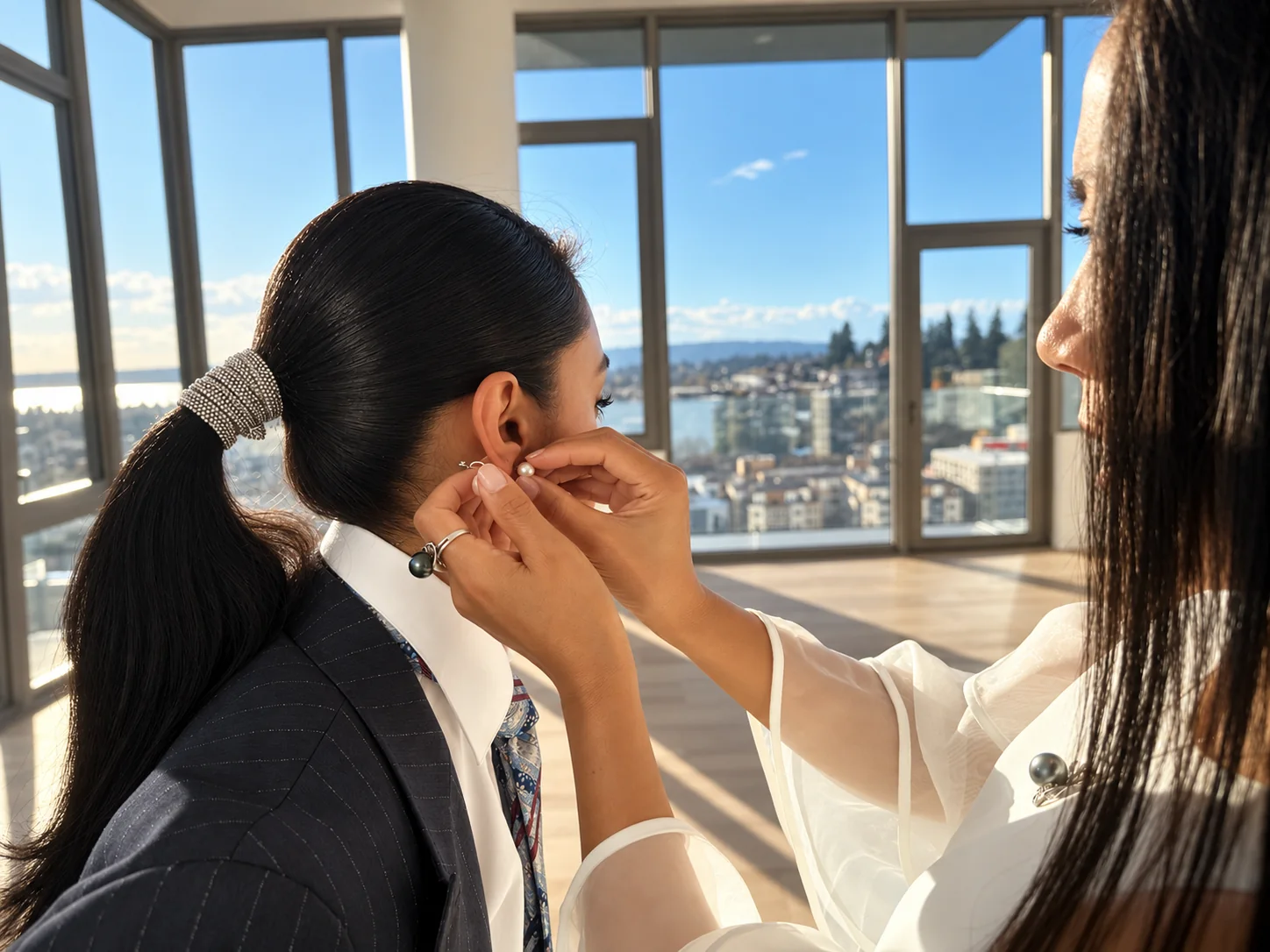 Holly Zhang fitting a pearl earring on a client beside tall windows overlooking Bellevue