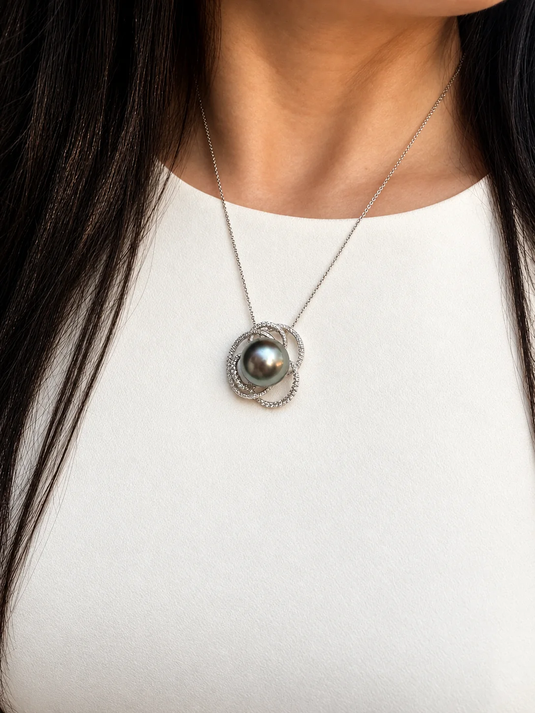 A Tahitian pearl pendant in a white swirl setting, worn over a white top