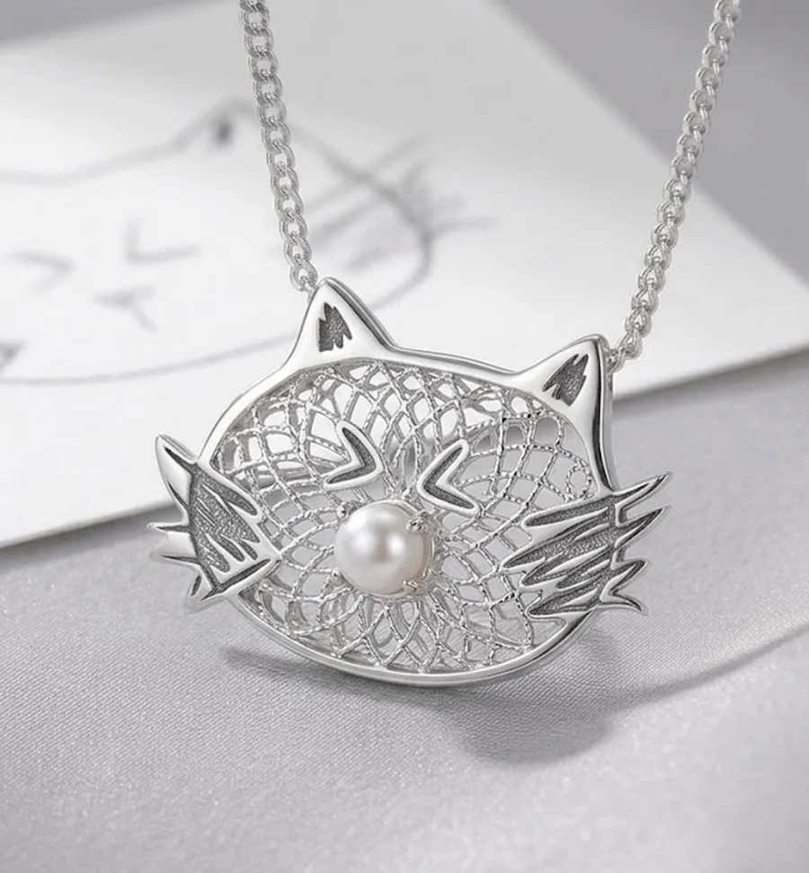 A silver filigree cat face pendant with a white pearl nose