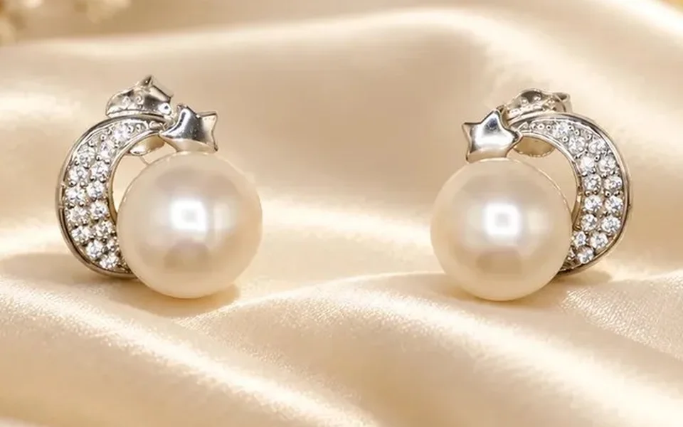 White pearl stud earrings set in pavé crescents on ivory silk