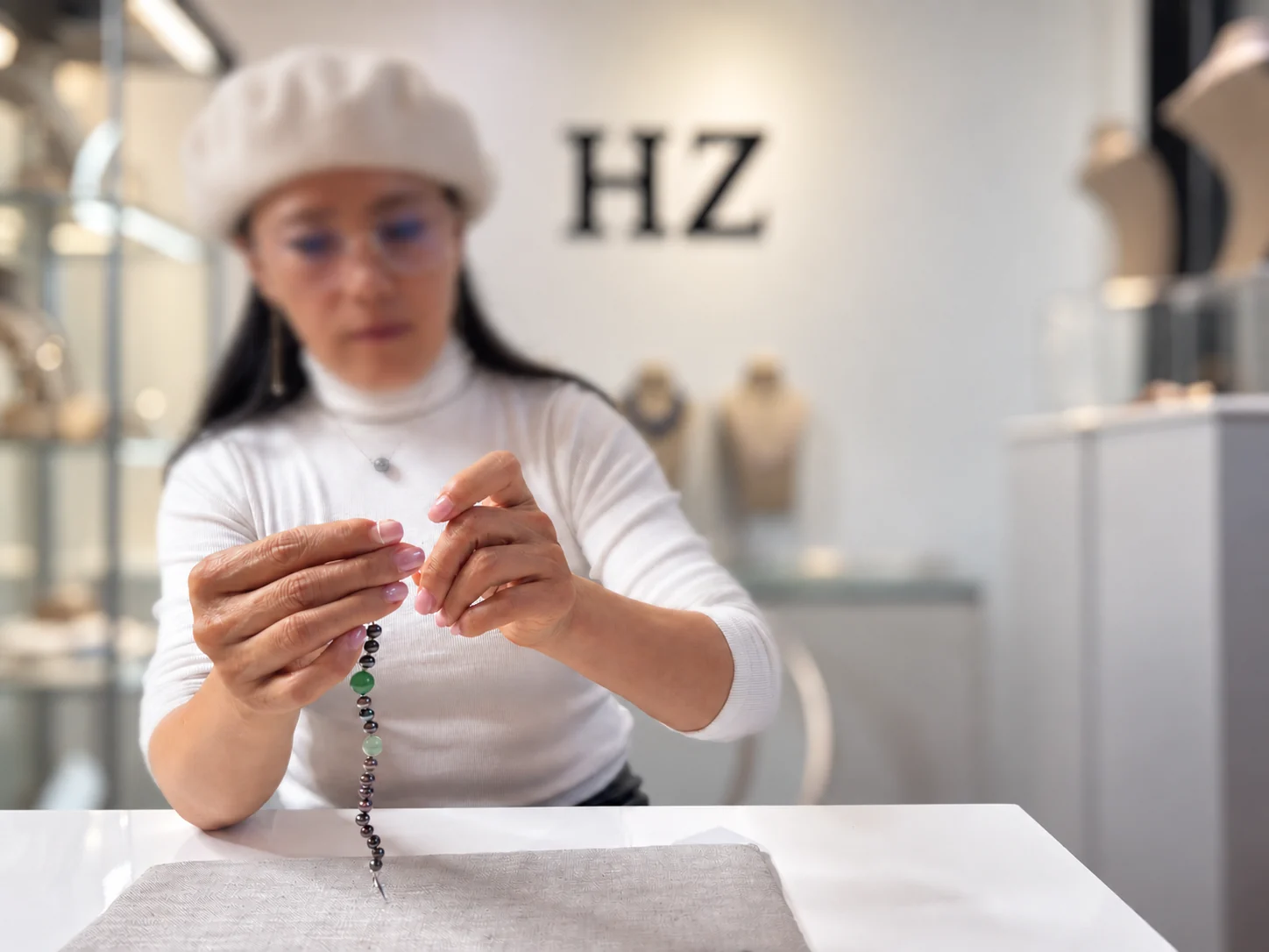 Holly Zhang restringing a strand of dark pearls and green jade at a table in the gallery