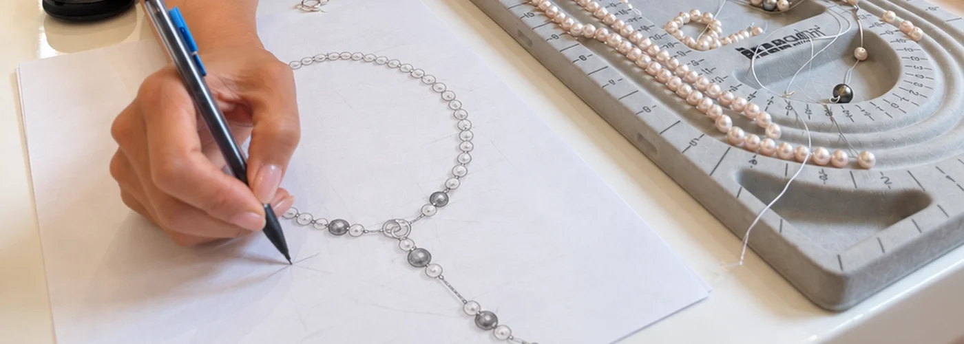 Holly sketching a pearl lariat at her bench, with strands laid out on a bead board