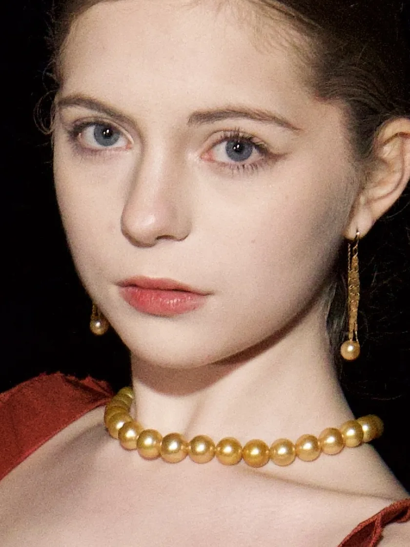 A woman wearing a golden South Sea pearl strand and long golden drop earrings